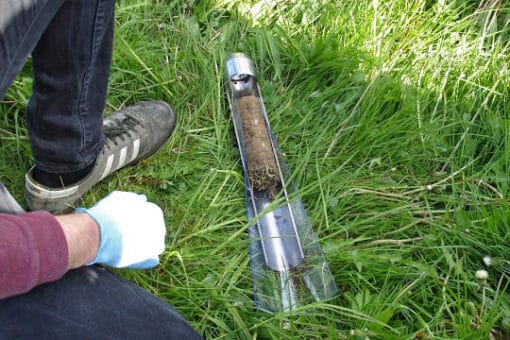 Figure: The photo shows the container of an earth boring rod lying in the tall grass of a meadow. The container contains a soil sample.