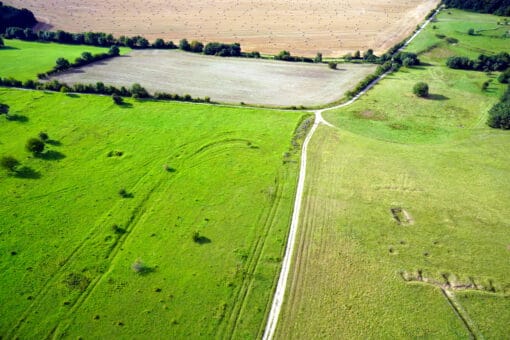 Abbildung: Die Drohnen-Aufnahme zeigt von oben fotografiert grüne Wiesen und braune Felder mit Wegen dazwischen.