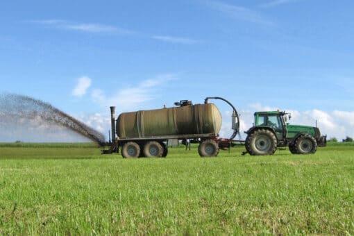 Abbildung: Das Foto zeigt einen Traktor mit angehängtem Gülletank beim Düngen einer kurzgemähten grünen Wiese.