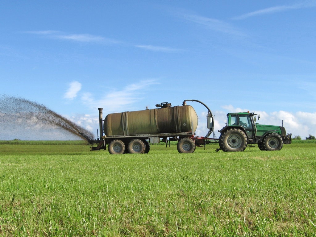 Abbildung: Das Foto zeigt einen Traktor mit angehängtem Gülletank beim Düngen einer kurzgemähten grünen Wiese.